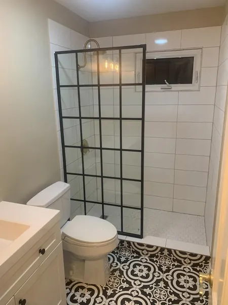 Tiled walk-in shower with a black grid glass panel and patterned floor tile