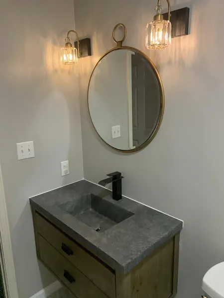 Floating wood vanity with a concrete top, round mirror and twin wall lights