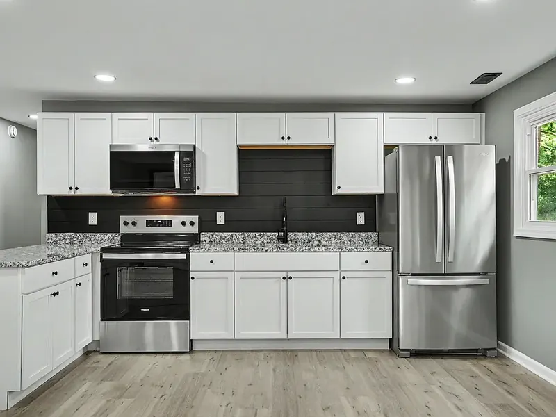 Kitchen with white shaker cabinets, a black plank backsplash, speckled granite counters, and a stainless steel range, microwave and French-door refrigerator on light wood-look flooring