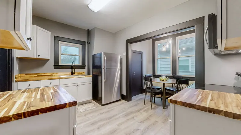 Kitchen with white shaker cabinets, butcher-block counters, a stainless refrigerator, a black faucet at the window sink, and a dining nook with a round table and chairs under pendant lights