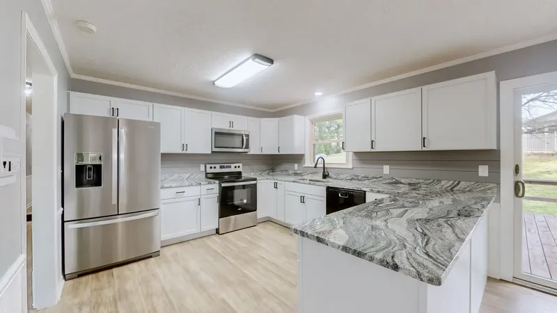 Kitchen with white shaker cabinets, gray swirled granite counters and peninsula, a stainless refrigerator, range and microwave, a black dishwasher, and a glass door to a deck