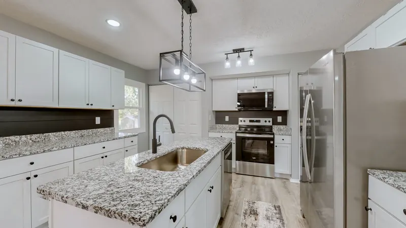 Kitchen with white shaker cabinets, speckled granite counters, an island with a stainless sink and black faucet, a black cage pendant light, and a stainless steel range, microwave and refrigerator